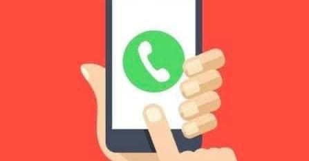 Hand holding a phone with WhatsApp on the screen.
